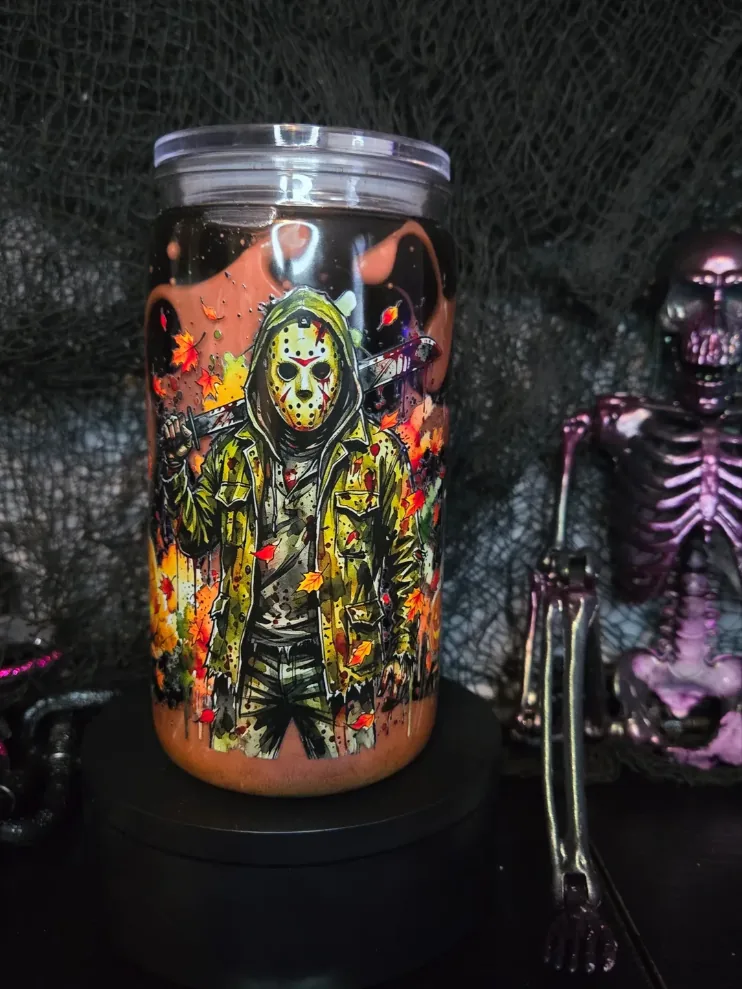 Rust-orange tumbler printed with a hockey-masked slasher in a green jacket surrounded by falling autumn leaves.